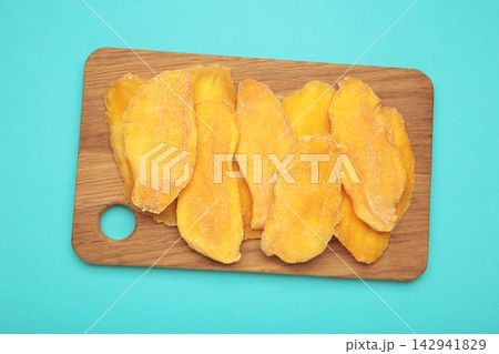 Slices of dried mango on cutting board on blue background. Slices of dried mango on cutting board on blue background. 142941829