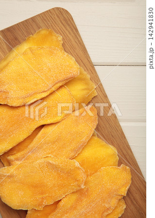 Slices of dried mango on cutting board on light wooden background. Vertical photo 142941830