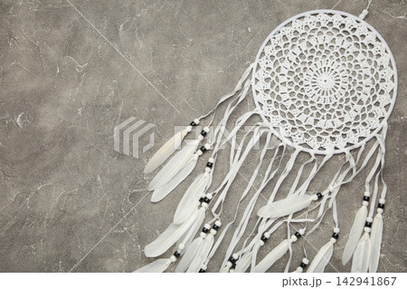 Handmade dream catcher hanging on a rope with feathers, threads, and beads on grey concrete background. 142941867
