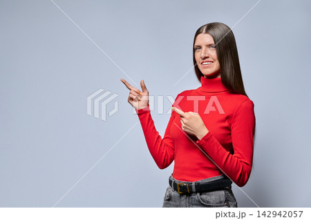 Smiling young woman pointing finger at copy space in studio portrait Smiling young woman pointing finger at copy space in studio portrait 142942057