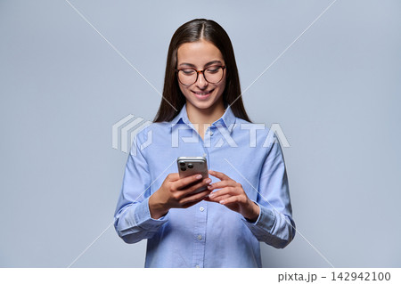 Young woman in glasses using smartphone smiling studio shot Young woman in glasses using smartphone smiling studio shot 142942100