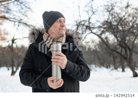 Mature man holding thermos in snowy winter park Mature man holding thermos in snowy winter park 142942514