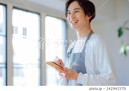 エプロン姿で注文をメモする笑顔の男性店員 エプロン姿で注文をメモする笑顔の男性店員 142942570