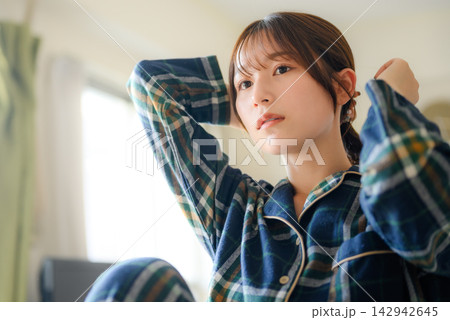 パジャマ姿の女性が髪を結ぶ、自宅での朝のヘアアレンジ パジャマ姿の女性が髪を結ぶ、自宅での朝のヘアアレンジ 142942645
