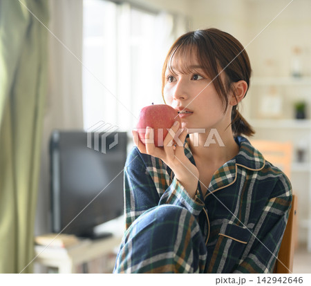 部屋着の女性がリンゴを食べる 部屋着の女性がリンゴを食べる 142942646