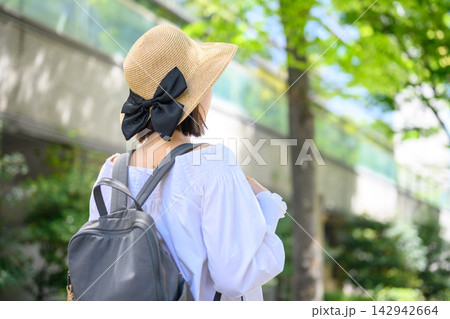 麦わら帽子とリュックの女性、新緑の街を散歩 142942664