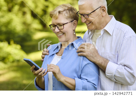 Senior couple laughing using smartphone in park, learning technology outdoors Senior couple laughing using smartphone in park, learning technology outdoors 142942771