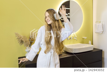 Happy woman in headphones singing and dancing in modern bathroom at home 142943032