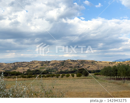 Dry farmland across rolling hills beneath cloudy sky Dry farmland across rolling hills beneath cloudy sky 142943275