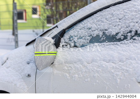 Snow-covered car uses reflective mirror cover and windshield protector to prevent frost and ice buildup during winter. Protective accessories help reduce scraping and improve cold-weather readiness Snow-covered car uses reflective mirror cover and windshield protector to prevent frost and ice buildup during winter. Protective accessories help reduce scraping and improve cold-weather readiness 142944004