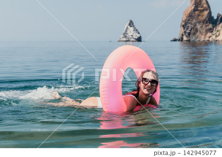 Swimming inflatable ring summer smiling woman enjoys her vacation while floating with a pink tube in clear sea water near cliffs 142945077