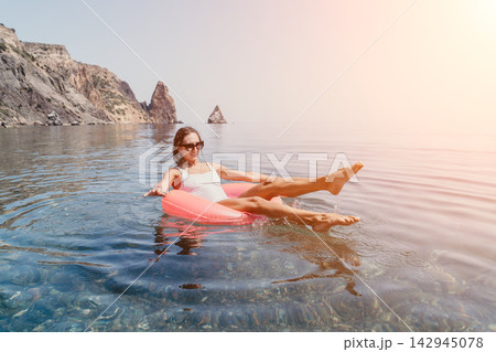 Woman floating ring happy young woman floating on pink inflatable ring in crystal clear sea water near rocky cliffs on sunny day Woman floating ring happy young woman floating on pink inflatable ring in crystal clear sea water near rocky cliffs on sunny day 142945078