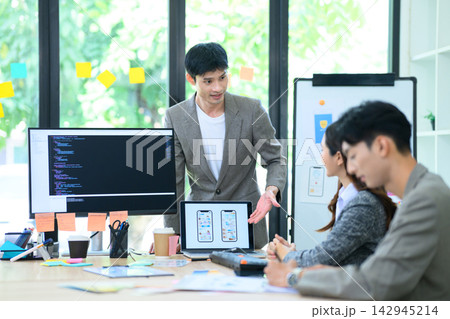 Asian Developer Presenting UI UX App Design to Team in Modern Office Meeting with Code on Monitor Asian Developer Presenting UI UX App Design to Team in Modern Office Meeting with Code on Monitor 142945214