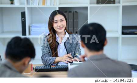 Smiling Asian businesswoman consulting with clients across office desk in professional meeting setting Smiling Asian businesswoman consulting with clients across office desk in professional meeting setting 142945225