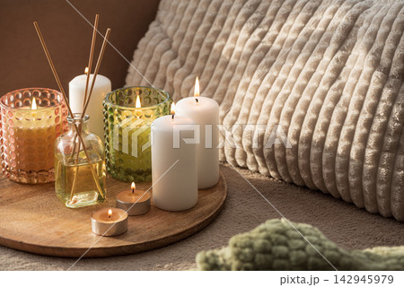 Group of lit candles and diffuser sticks arranged on a wooden tray with textured pillows Group of lit candles and diffuser sticks arranged on a wooden tray with textured pillows 142945979