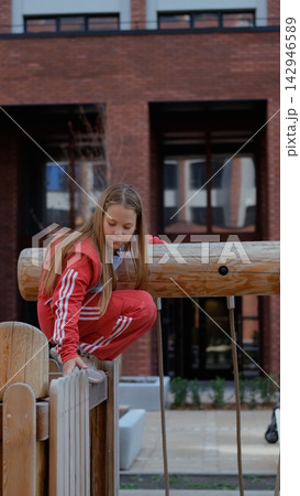 Focused girl balancing on a wooden playground structure, taking on a physical challenge and building confidence through outdoor play 142946589