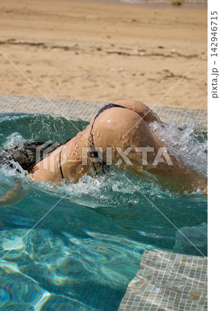 a girl with a beautiful tanned body having fun in the swimming pool of a luxury villa, the girl's butt is visible from under the water, azure water, splashes of water glow in the sun 142946715