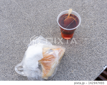 Plastic cup of hot tea and a sandwich in a bag on a textured stone surface. Takeaway breakfast or snack concept Plastic cup of hot tea and a sandwich in a bag on a textured stone surface. Takeaway breakfast or snack concept 142947493