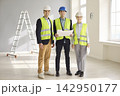 Confident engineers and contractors review blueprints in safety gear indoors 142950177