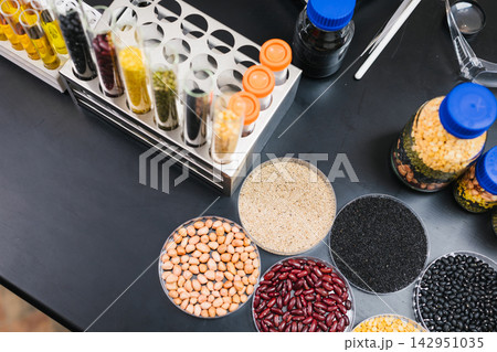Top view of laboratory samples with test tubes and bowls of beans, seeds, grains, and powders on a dark work table. Top view of laboratory samples with test tubes and bowls of beans, seeds, grains, and powders on a dark work table. 142951035