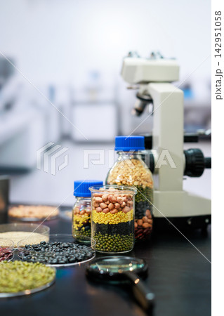 Jars of colorful beans, grains and seeds beside a microscope in a laboratory, food research, nutrition testing and agricultural quality control. Jars of colorful beans, grains and seeds beside a microscope in a laboratory, food research, nutrition testing and agricultural quality control. 142951058