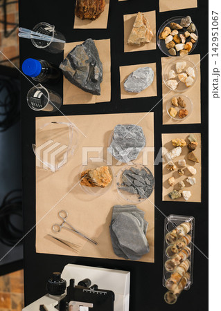 Top view of a geology worktable with labeled rock samples, crystals, shells, magnifier, tweezers and storage containers on black and brown paper. Top view of a geology worktable with labeled rock samples, crystals, shells, magnifier, tweezers and storage containers on black and brown paper. 142951067