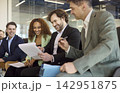 Smiling business team in office meeting reviewing papers and planning strategy 142951875