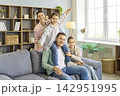 Smiling mother and father with daughters playing on sofa in bright home interior 142951995