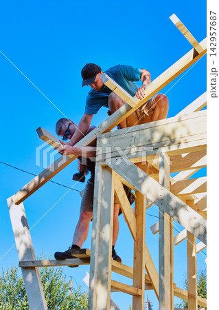 Installation of rafter system of timber frame house, workers fastening rafter leg while holding it together. Installation of rafter system of timber frame house, workers fastening rafter leg while holding it together. 142957687