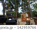 木立の中のキャンプサイトにランタンと椅子のアウトドア風景 142959766