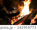 焚き火の炎の中で調理器具に料理するキャンプシーン 142959773
