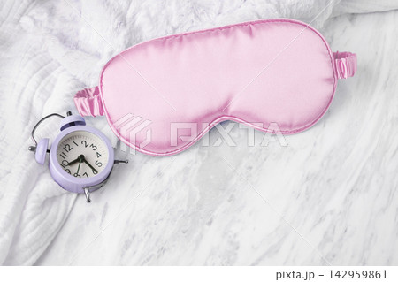 Pink sleep mask and alarm clock on soft towel on white marble background 142959861