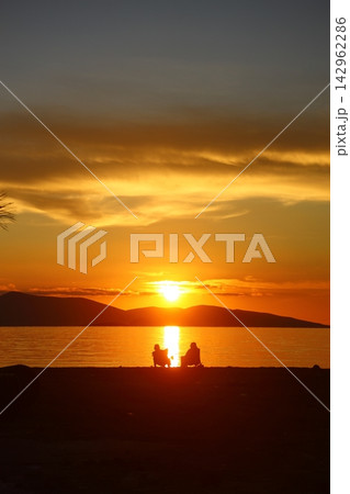 two people talking by the sea at sunset and a lonely fishing boat in the sea two people talking by the sea at sunset and a lonely fishing boat in the sea 142962286