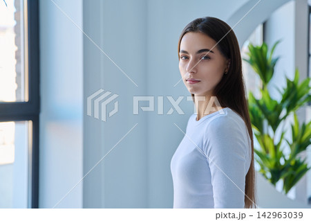 Portrait of serious young woman standing near window side view 142963039
