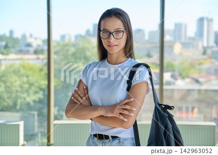 Smiling female student wearing eyeglasses with crossed arms against city window 142963052