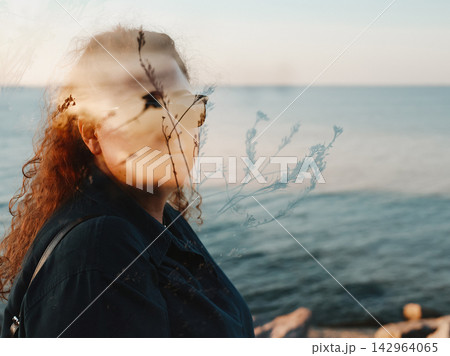Dreamy portrait of a woman wearing sunglasses near the sea, with fine wild plants layered across her face in double exposure, creating a soft atmospheric summer scene about nature, freedom and escape. 142964065