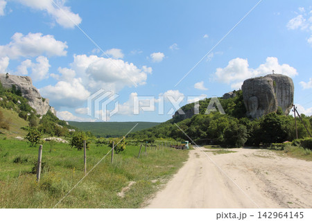 Sunlit dirt path winds through green fields and rocky cliffs Sunlit dirt path winds through green fields and rocky cliffs 142964145