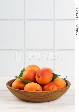 Fresh ripe apricots in wooden bowl on white kitchen table and white tiled wall with copy space 142964180