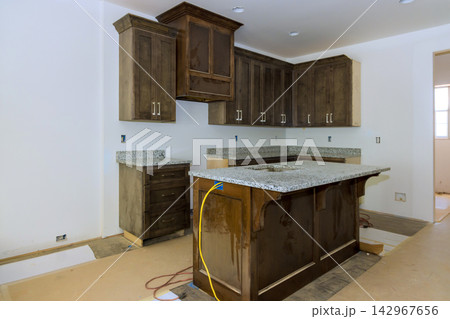 Workers are installing wooden cabinets granite countertops in kitchen space is unfinished empty. 142967656