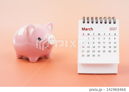 Desk calendar for March 2027 and pink piggy bank. 142968468