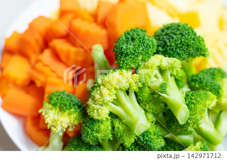 Broccoli and carrot pieces on white plate with fresh vegetables 142971712