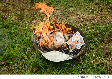 Ritual of burning joss paper, also known as ghost money, inside a metal container placed on the grass. 142972384