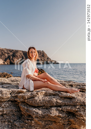Woman beach vacation sitting on coastal rocks overlooking the blue sea during summer sunset holiday with copy space Woman beach vacation sitting on coastal rocks overlooking the blue sea during summer sunset holiday with copy space 142973032