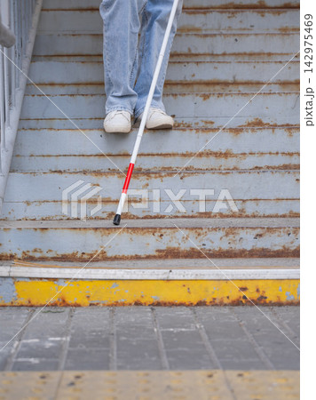 A blind woman descends a staircase. Close-up of her feet and a tactile stick. A blind woman descends a staircase. Close-up of her feet and a tactile stick. 142975469