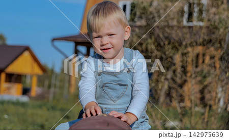 Toddler boy smiling while playing outdoors on wooden seesaw in sunny backyard, with toddler, boy, child, smiling detail, showing playing, seesaw, playground, overall context, with clear visible detail Toddler boy smiling while playing outdoors on wooden seesaw in sunny backyard, with toddler, boy, child, smiling detail, showing playing, seesaw, playground, overall context, with clear visible detail 142975639