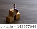 Businesswoman figurine sitting on wooden blocks representing career growth 142977044