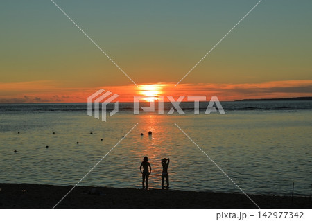 夕暮れ時の沖縄の瀬底ビーチで沈み行く夕日を見つめる女性 夕暮れ時の沖縄の瀬底ビーチで沈み行く夕日を見つめる女性 142977342