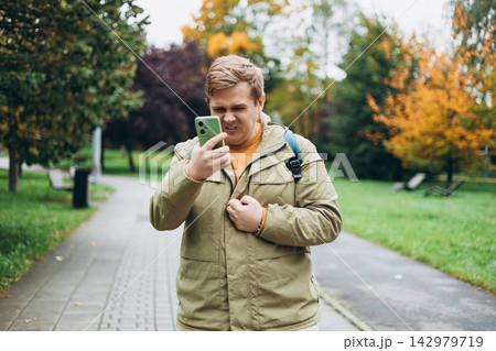 Perplexed man holding cellphone in hands on the street, looking at screen with irritated expression, made a mistake or annoyed by texts and calls. Negative emotion. High quality photo Perplexed man holding cellphone in hands on the street, looking at screen with irritated expression, made a mistake or annoyed by texts and calls. Negative emotion. High quality photo 142979719