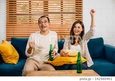 Excited young couple celebrates victory while watching TV their cheers filling the room with happiness Excited young couple celebrates victory while watching TV their cheers filling the room with happiness 142980461
