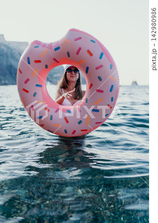 Woman, inflatable, ocean. Cheerful woman enjoys summer vacation looking through pink donut ring in clear blue sea. Woman, inflatable, ocean. Cheerful woman enjoys summer vacation looking through pink donut ring in clear blue sea. 142980986